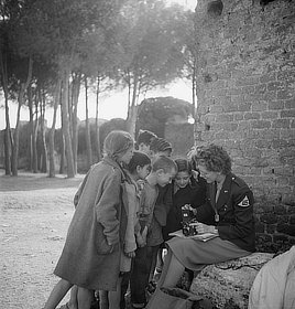 Toni Frissell, photographer, with children looking at her camera. World War II photo, 1945.